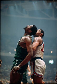 Color photograph of two bascketball players looking up in the same direction at something not visible in the image.
